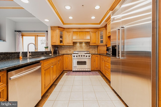 kitchen with sink, crown molding, high quality appliances, dark stone counters, and decorative backsplash