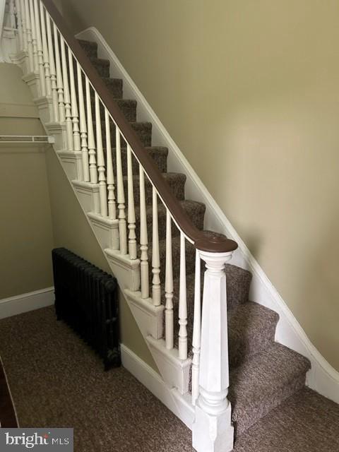 staircase with carpet floors, radiator heating unit, and baseboards