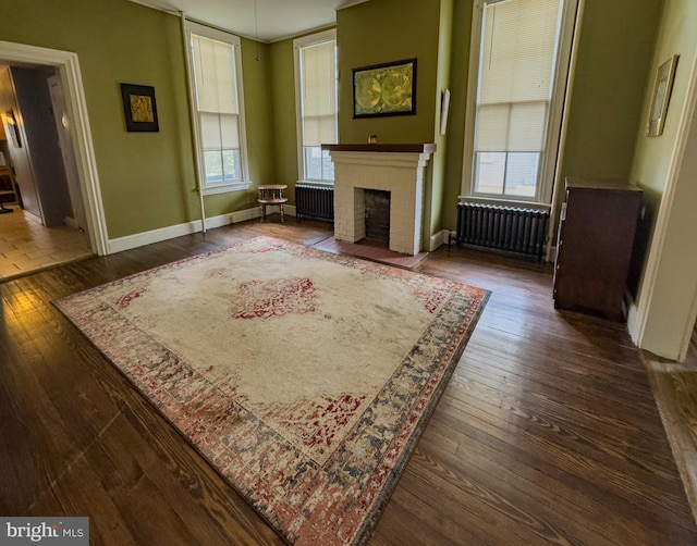 unfurnished living room featuring dark wood-type flooring, radiator heating unit, a brick fireplace, and baseboards