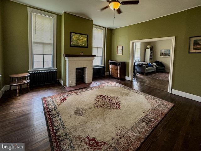 living area with a brick fireplace, baseboards, radiator heating unit, and wood finished floors