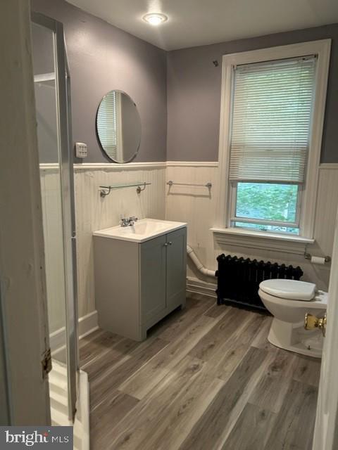 bathroom with toilet, a wainscoted wall, wood finished floors, vanity, and radiator