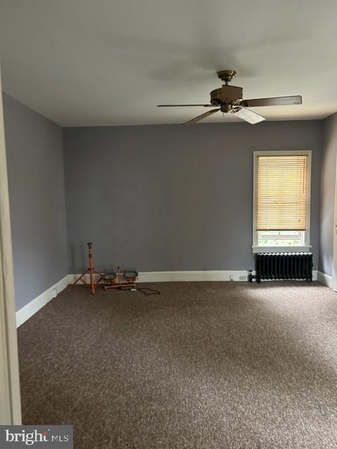 unfurnished room with radiator, ceiling fan, baseboards, and carpet flooring