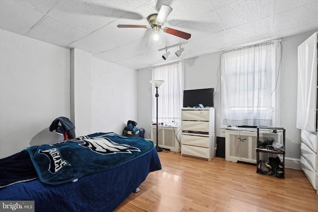 bedroom featuring hardwood / wood-style flooring, a drop ceiling, ceiling fan, and multiple windows