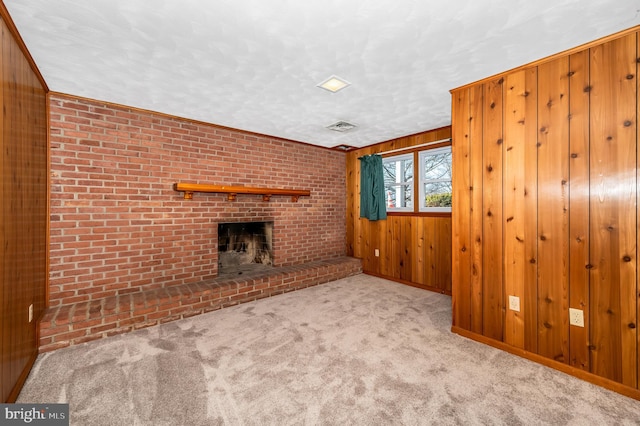 unfurnished living room with a textured ceiling, wooden walls, light colored carpet, brick wall, and a fireplace