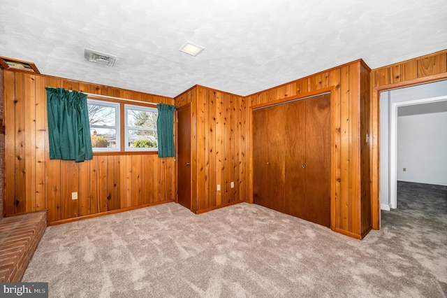 unfurnished room featuring light colored carpet, a textured ceiling, and wood walls