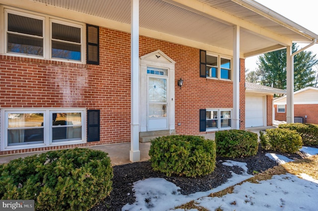 snow covered property entrance featuring a garage and a porch