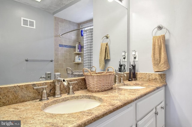 full bath featuring visible vents, a sink, a tile shower, and double vanity