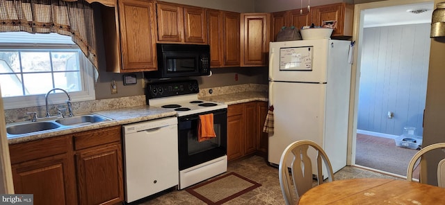 kitchen featuring white appliances, wooden walls, brown cabinets, light countertops, and a sink