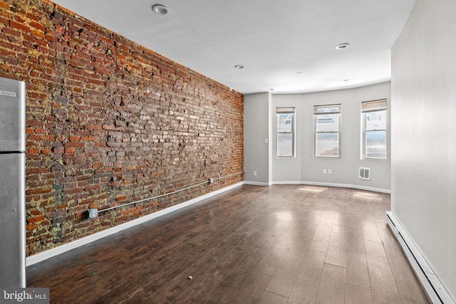 empty room featuring brick wall, a baseboard heating unit, and dark hardwood / wood-style floors