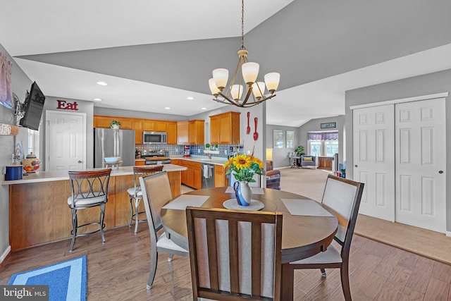 dining space featuring an inviting chandelier, light hardwood / wood-style floors, and vaulted ceiling