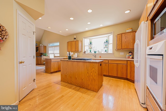 kitchen with a center island, vaulted ceiling, light hardwood / wood-style flooring, and oven