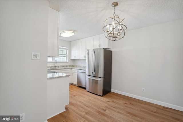 kitchen featuring decorative light fixtures, a textured ceiling, stainless steel appliances, light hardwood / wood-style floors, and white cabinets