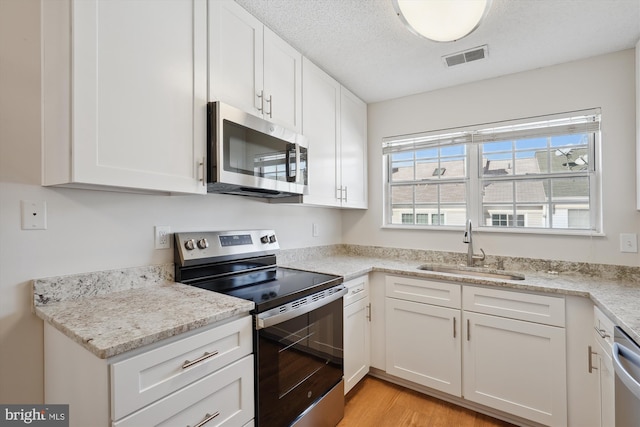 kitchen featuring sink, light wood-type flooring, white cabinets, stainless steel appliances, and a textured ceiling