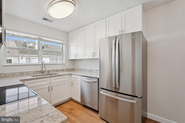 kitchen with sink, light hardwood / wood-style flooring, white cabinetry, stainless steel appliances, and light stone countertops