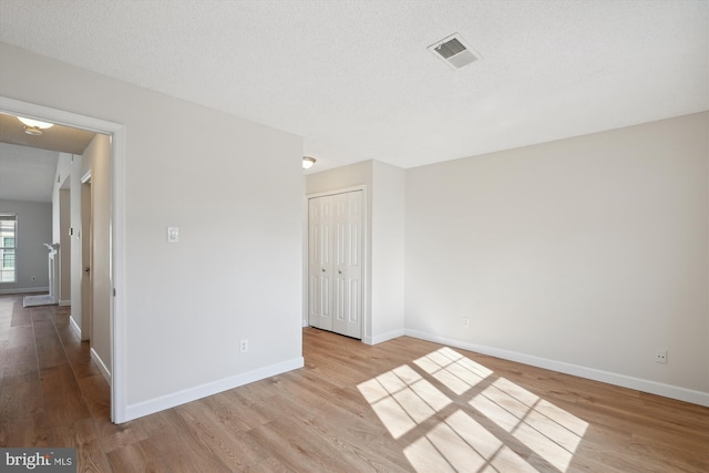 unfurnished room with a textured ceiling and light wood-type flooring