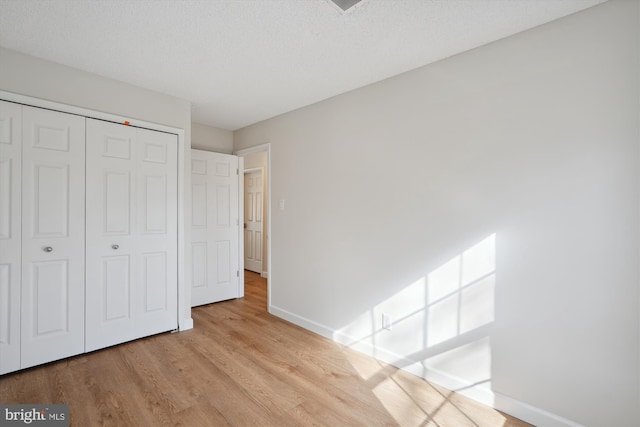 unfurnished bedroom featuring a textured ceiling, light wood-type flooring, and a closet