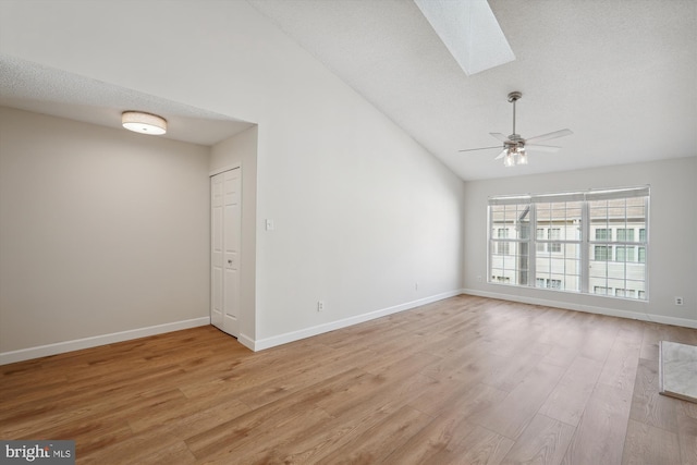 unfurnished room featuring ceiling fan, vaulted ceiling with skylight, a textured ceiling, and light hardwood / wood-style floors