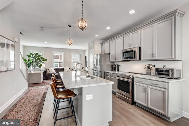 kitchen featuring appliances with stainless steel finishes, open floor plan, a sink, and gray cabinetry