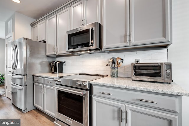 kitchen featuring tasteful backsplash, a toaster, light wood-style flooring, gray cabinets, and stainless steel appliances