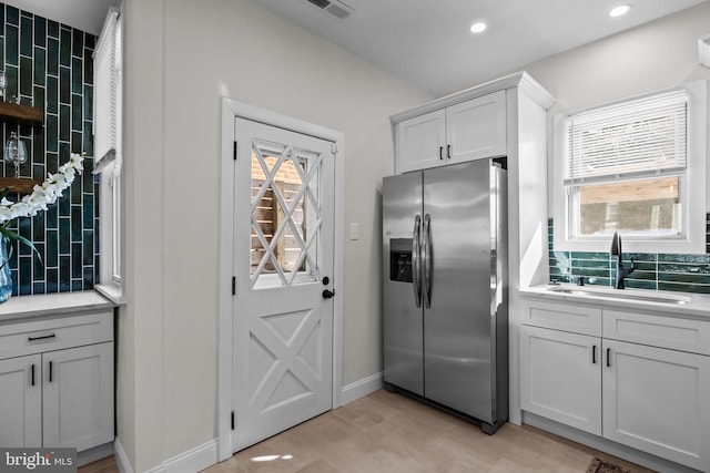 kitchen with stainless steel fridge with ice dispenser, a wealth of natural light, sink, and white cabinets