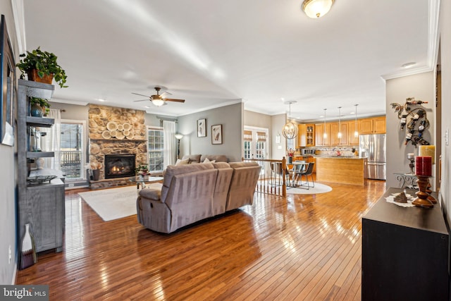 living room with crown molding, a stone fireplace, ceiling fan, and hardwood / wood-style flooring