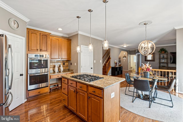 kitchen featuring dark wood-type flooring, stainless steel appliances, a center island, light stone countertops, and decorative light fixtures