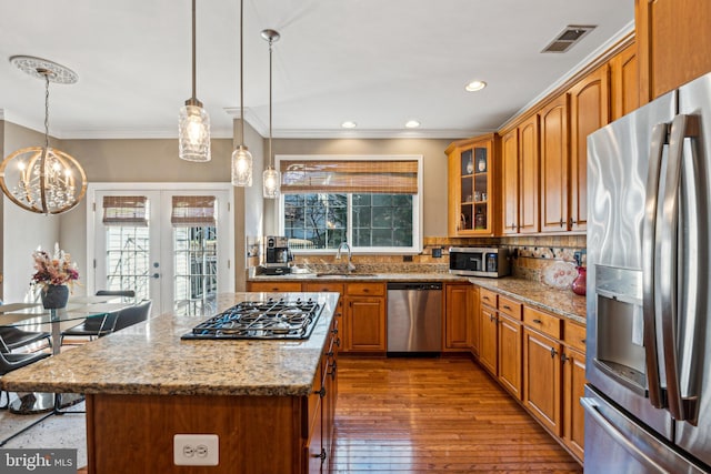 kitchen featuring sink, light stone counters, appliances with stainless steel finishes, a kitchen island, and pendant lighting