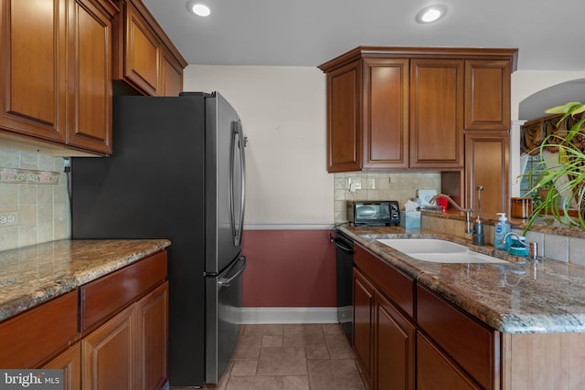 kitchen with sink, black dishwasher, stainless steel fridge, light stone countertops, and decorative backsplash