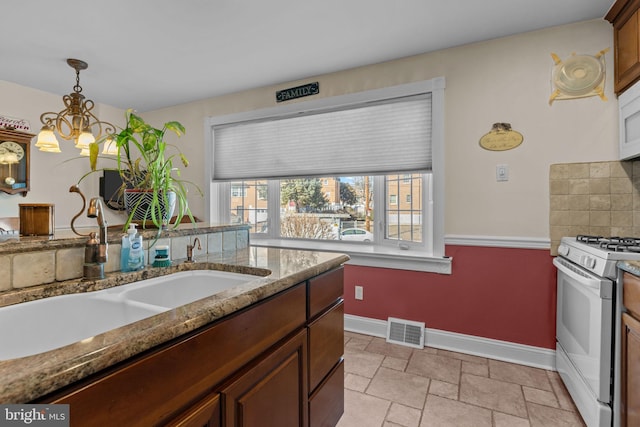 kitchen featuring hanging light fixtures, sink, backsplash, white appliances, and light stone counters