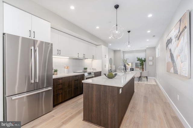 kitchen with dark brown cabinetry, decorative light fixtures, a center island with sink, light wood-type flooring, and stainless steel fridge