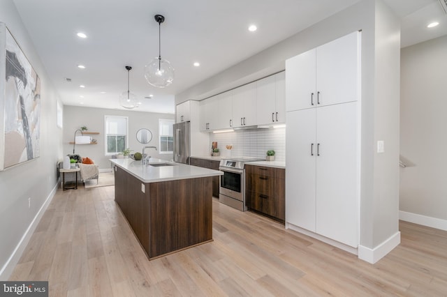 kitchen with sink, hanging light fixtures, dark brown cabinets, a center island with sink, and appliances with stainless steel finishes