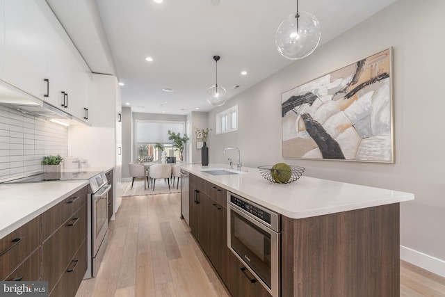 kitchen featuring sink, hanging light fixtures, an island with sink, stainless steel appliances, and white cabinets