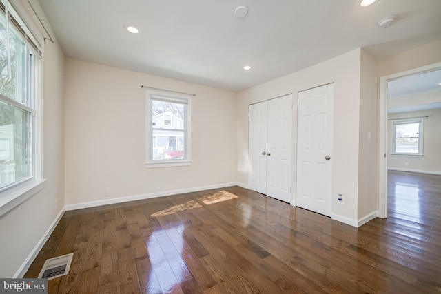 unfurnished bedroom featuring dark hardwood / wood-style flooring and two closets