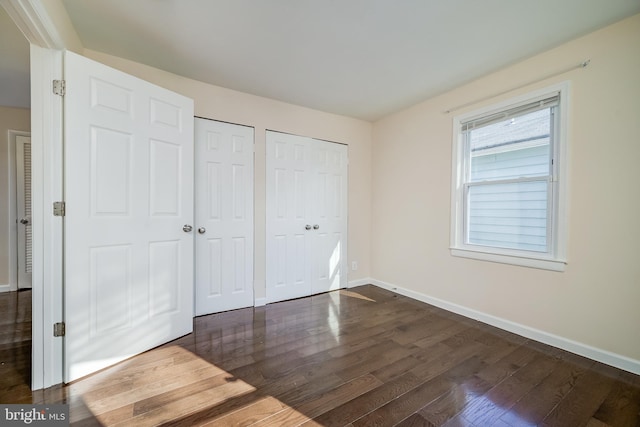 unfurnished bedroom featuring two closets and dark hardwood / wood-style floors