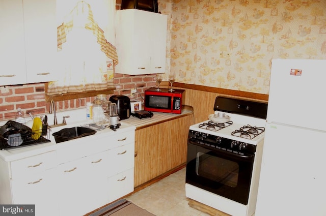 kitchen with white refrigerator, white cabinetry, range with gas stovetop, and sink