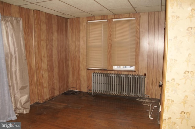 unfurnished room with a drop ceiling, radiator, wooden walls, and dark hardwood / wood-style floors