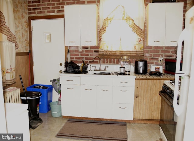 kitchen featuring sink, white cabinetry, radiator heating unit, range with gas stovetop, and brick wall