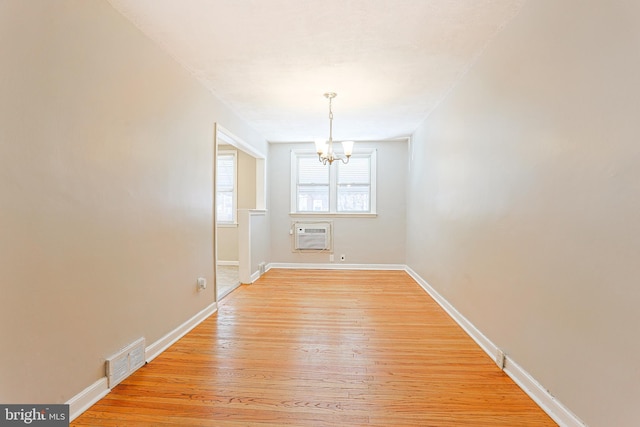 unfurnished room with an inviting chandelier, light wood-type flooring, and an AC wall unit