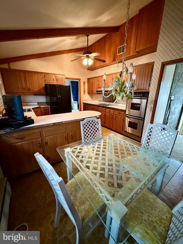 kitchen with brown cabinetry, wallpapered walls, light countertops, beamed ceiling, and black fridge