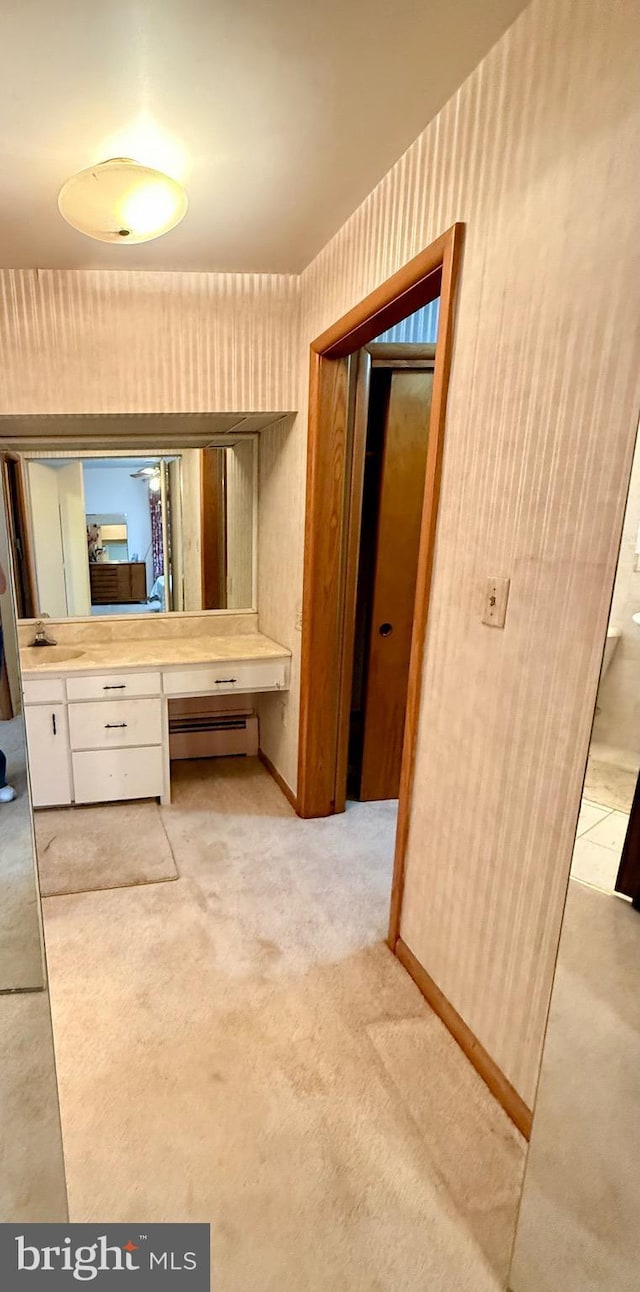 bathroom featuring a sink, a baseboard radiator, baseboards, and wallpapered walls