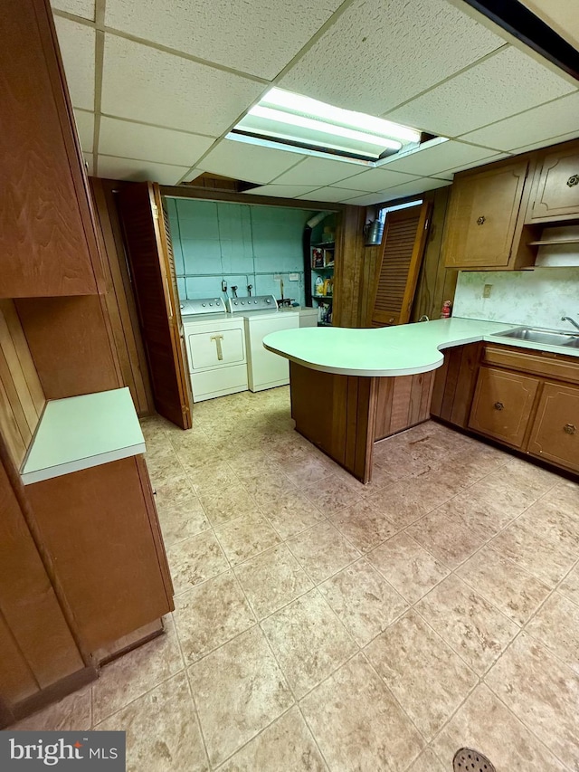 kitchen featuring washing machine and clothes dryer, a peninsula, a drop ceiling, a sink, and light countertops