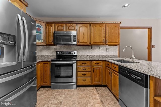 kitchen with sink, appliances with stainless steel finishes, tasteful backsplash, light stone countertops, and kitchen peninsula