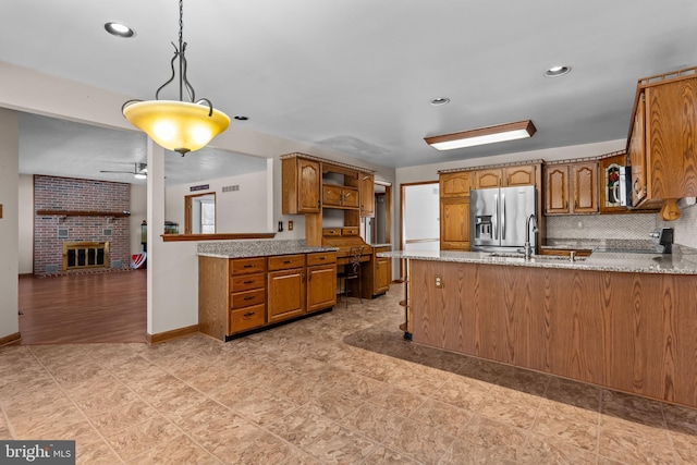 kitchen featuring sink, decorative light fixtures, kitchen peninsula, stainless steel appliances, and a fireplace