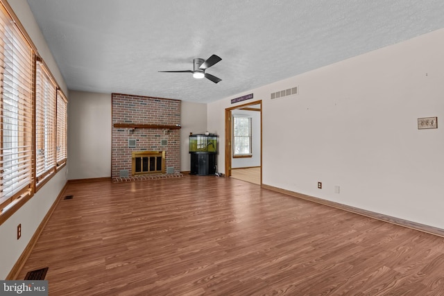 unfurnished living room featuring a brick fireplace, hardwood / wood-style floors, and a textured ceiling