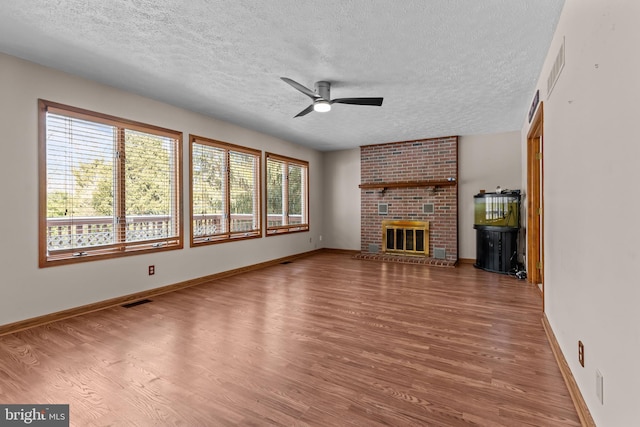 unfurnished living room with a brick fireplace, hardwood / wood-style flooring, a textured ceiling, and ceiling fan