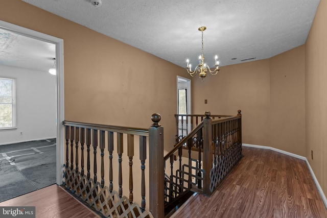 staircase with hardwood / wood-style flooring, a textured ceiling, and a notable chandelier