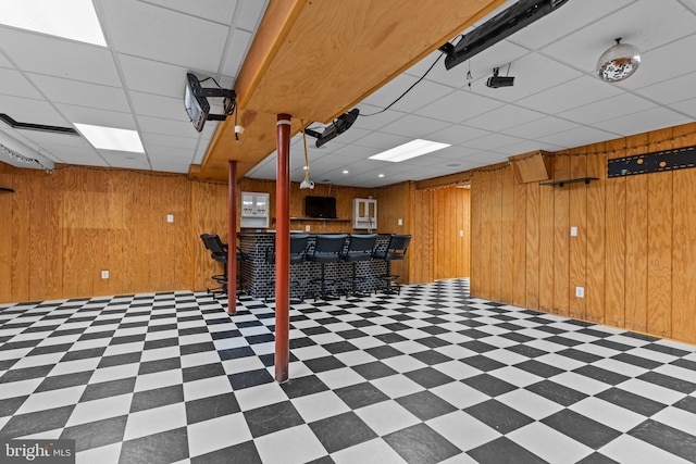 basement with a drop ceiling, bar, and wood walls