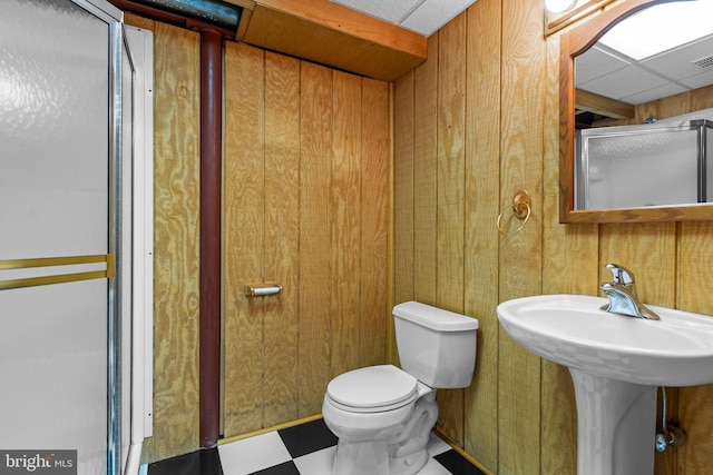 bathroom with wooden walls, toilet, and a drop ceiling