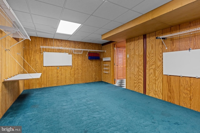 basement with carpet flooring, a paneled ceiling, and wood walls