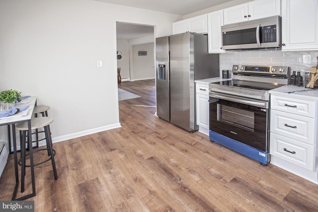 kitchen featuring light hardwood / wood-style flooring, stainless steel appliances, light stone countertops, decorative backsplash, and white cabinets